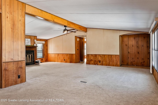 unfurnished living room with lofted ceiling with beams, carpet floors, ceiling fan, and wood walls