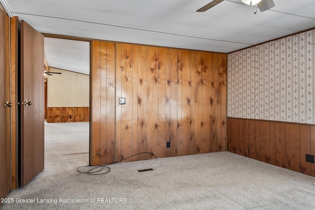 spare room with ceiling fan, light colored carpet, and wooden walls