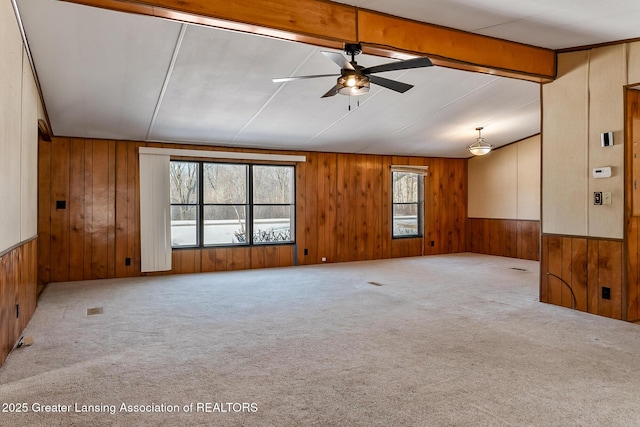 carpeted empty room with plenty of natural light, lofted ceiling with beams, ceiling fan, and wood walls