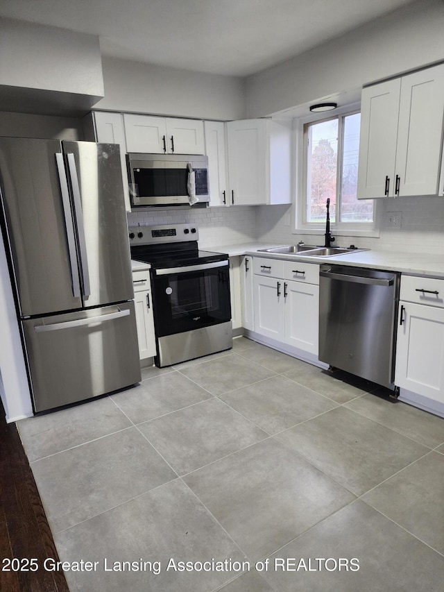 kitchen with tasteful backsplash, white cabinetry, sink, light tile patterned floors, and stainless steel appliances