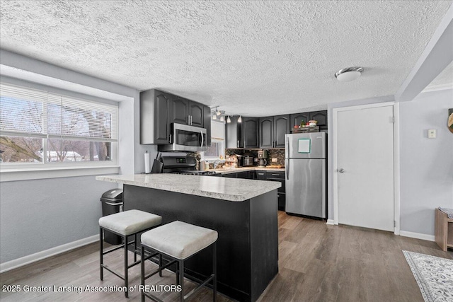 kitchen with stainless steel appliances, dark hardwood / wood-style floors, a breakfast bar, and kitchen peninsula