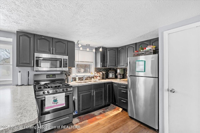 kitchen featuring sink, appliances with stainless steel finishes, wood-type flooring, a textured ceiling, and decorative backsplash