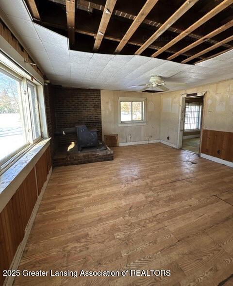 unfurnished living room featuring hardwood / wood-style flooring, ceiling fan, and wooden walls