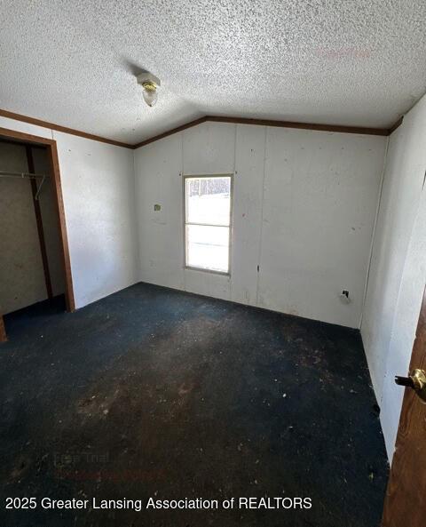 unfurnished bedroom with crown molding, vaulted ceiling, a closet, and a textured ceiling