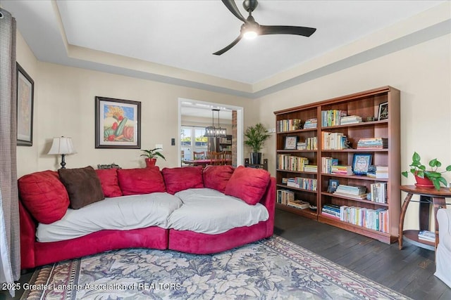 living area featuring dark wood-type flooring, ceiling fan, and a raised ceiling