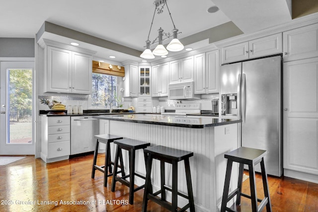 kitchen with appliances with stainless steel finishes, a breakfast bar, white cabinets, decorative backsplash, and hardwood / wood-style flooring