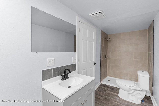 bathroom with vanity, hardwood / wood-style flooring, toilet, and tiled shower