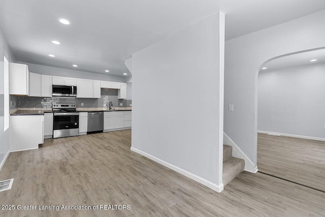 kitchen featuring white cabinetry, backsplash, stainless steel appliances, and light hardwood / wood-style floors