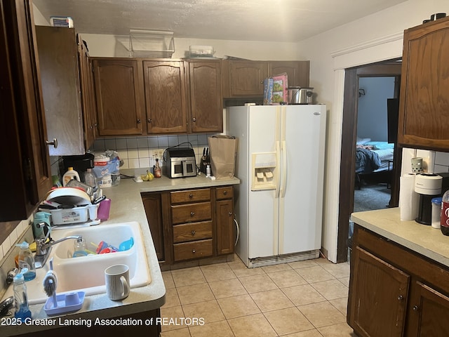 kitchen featuring sink, decorative backsplash, white fridge with ice dispenser, light tile patterned floors, and dark brown cabinets