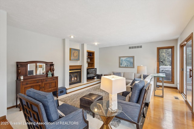 living room featuring a textured ceiling, light hardwood / wood-style floors, and built in shelves