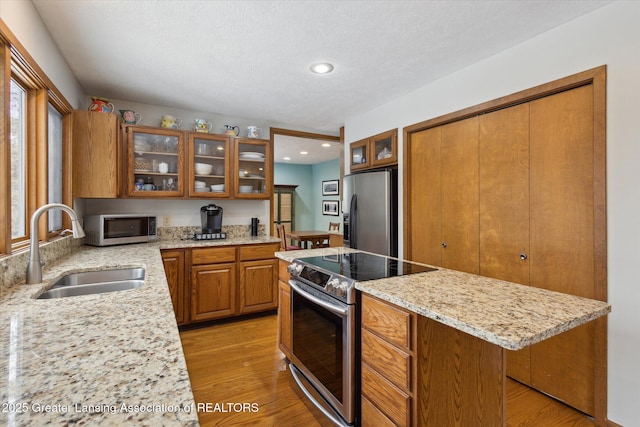 kitchen featuring a kitchen island, appliances with stainless steel finishes, sink, light stone countertops, and light hardwood / wood-style flooring