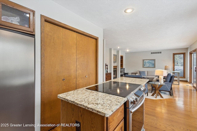 kitchen featuring stainless steel electric range oven, light stone counters, a textured ceiling, and light wood-type flooring