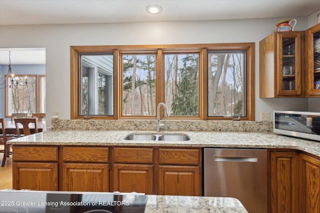 kitchen featuring sink, appliances with stainless steel finishes, hanging light fixtures, light stone counters, and a notable chandelier