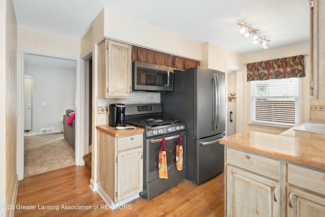 kitchen featuring backsplash, light brown cabinets, light hardwood / wood-style floors, and appliances with stainless steel finishes