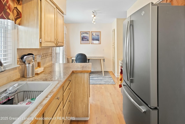 kitchen with sink, backsplash, stainless steel fridge, light brown cabinets, and light wood-type flooring