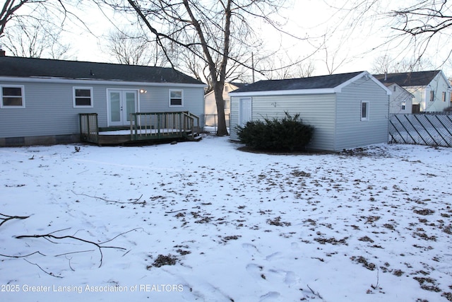 snow covered rear of property with french doors and a deck