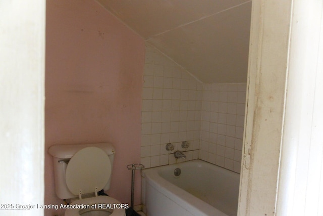 bathroom with toilet, a bath, and vaulted ceiling