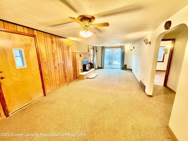 unfurnished living room featuring light colored carpet, ceiling fan, and wood walls