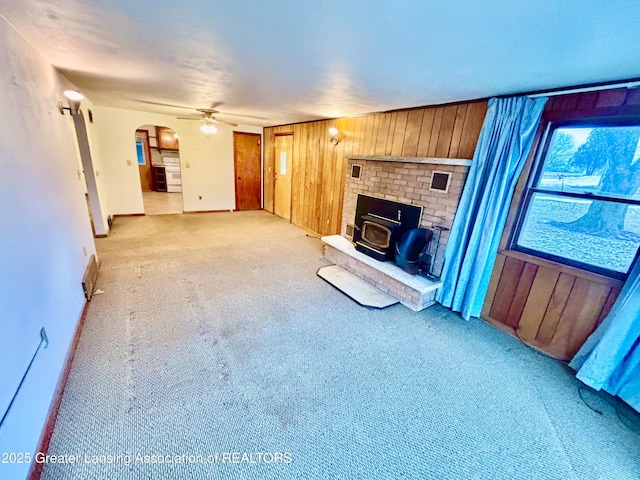 unfurnished living room with a wood stove, light colored carpet, ceiling fan, and wood walls