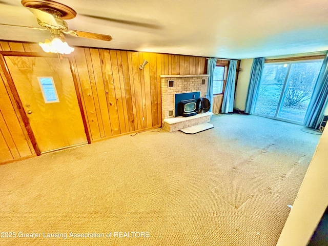 unfurnished living room with wooden walls, ceiling fan, and carpet flooring