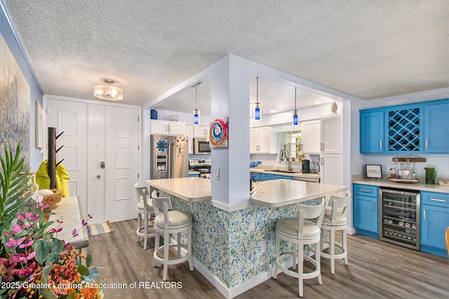 kitchen with a breakfast bar, pendant lighting, blue cabinets, beverage cooler, and stainless steel appliances