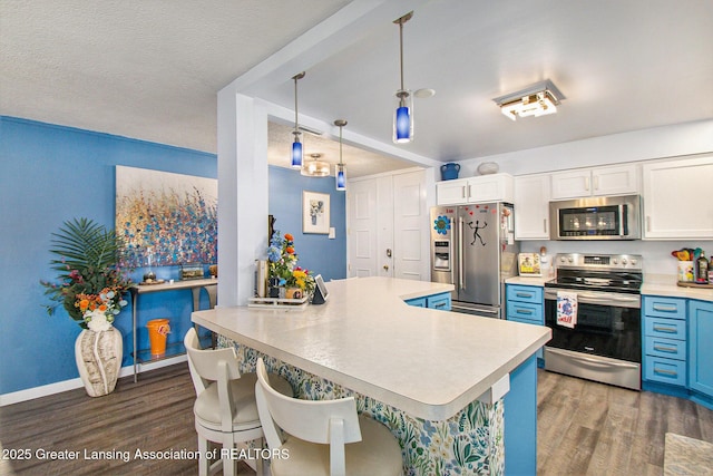 kitchen with white cabinets, dark hardwood / wood-style flooring, a kitchen bar, hanging light fixtures, and stainless steel appliances