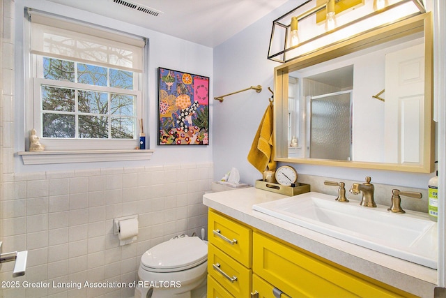 bathroom with vanity, toilet, a shower with door, and tile walls