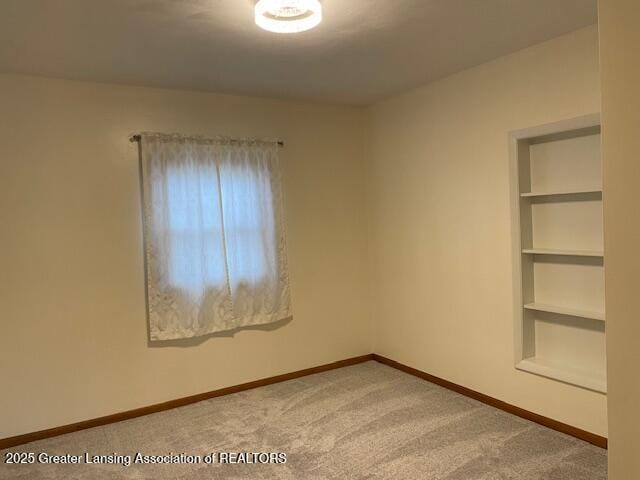 carpeted spare room featuring baseboards and built in features