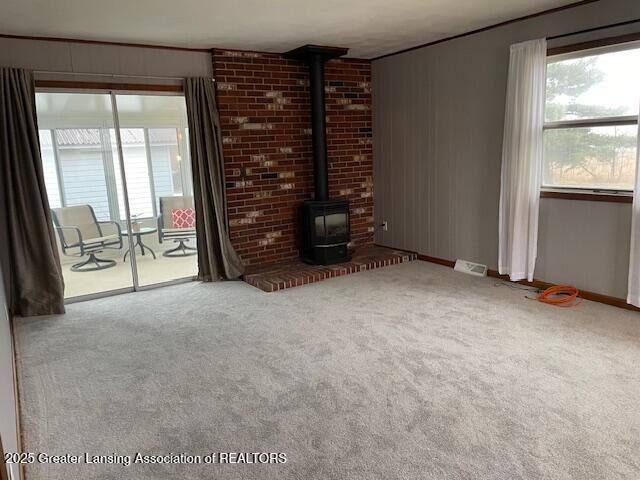 unfurnished living room featuring carpet, a wood stove, and a healthy amount of sunlight