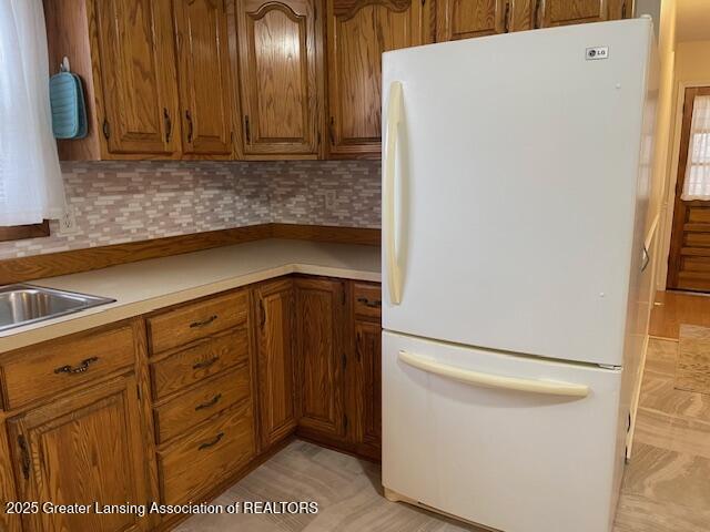 kitchen featuring a sink, light countertops, freestanding refrigerator, decorative backsplash, and brown cabinetry