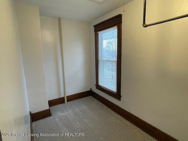 carpeted empty room featuring attic access and baseboards