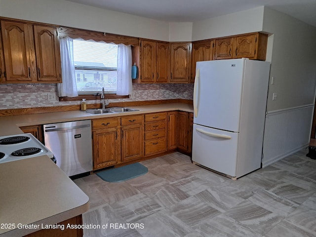 kitchen featuring light countertops, brown cabinetry, freestanding refrigerator, a sink, and dishwasher