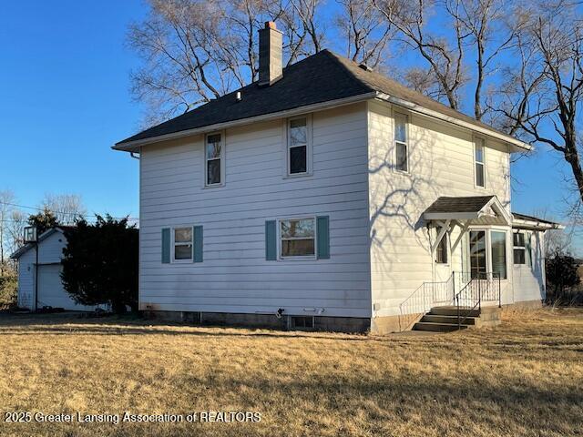 rear view of house featuring a yard, a chimney, and an outdoor structure