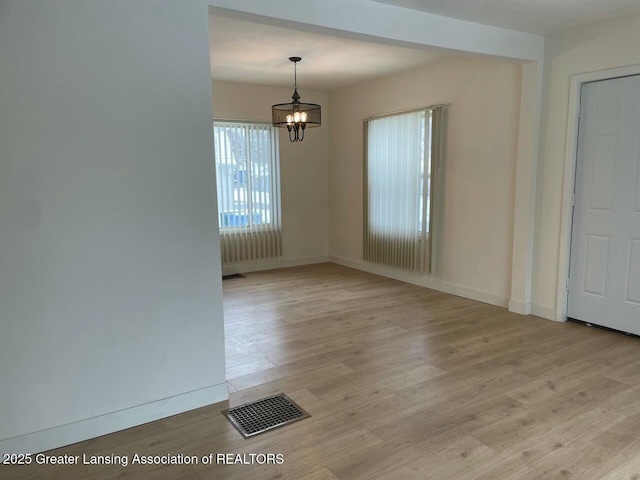 empty room with light hardwood / wood-style floors and a notable chandelier