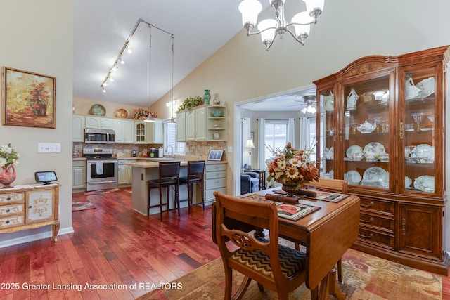 dining space with dark hardwood / wood-style floors, ceiling fan with notable chandelier, high vaulted ceiling, sink, and track lighting