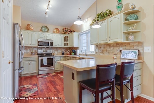 kitchen featuring a breakfast bar area, appliances with stainless steel finishes, decorative light fixtures, vaulted ceiling, and kitchen peninsula