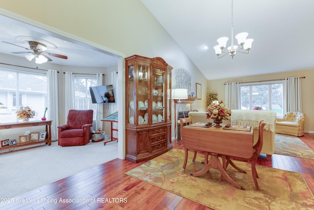 dining area with hardwood / wood-style flooring, ceiling fan with notable chandelier, and high vaulted ceiling