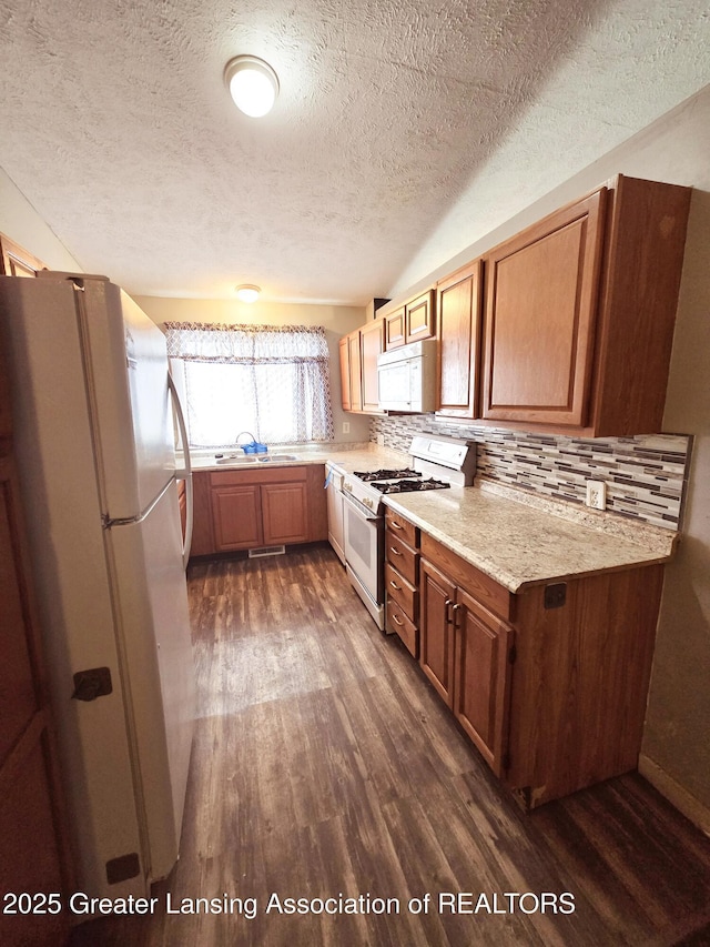 kitchen featuring sink, dark hardwood / wood-style floors, white appliances, light stone countertops, and decorative backsplash