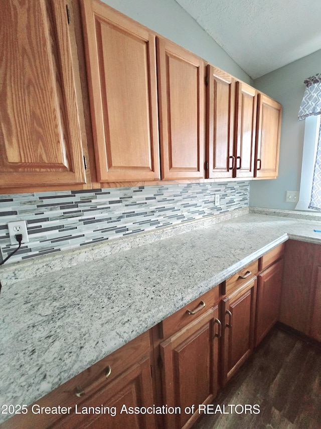 kitchen featuring lofted ceiling, decorative backsplash, light stone countertops, and a textured ceiling