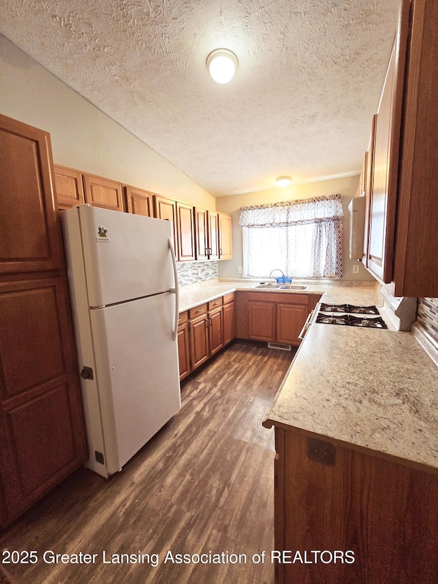 kitchen with vaulted ceiling, dark hardwood / wood-style floors, sink, white appliances, and a textured ceiling