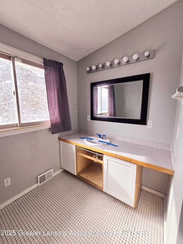 bathroom with lofted ceiling, sink, a textured ceiling, and a healthy amount of sunlight