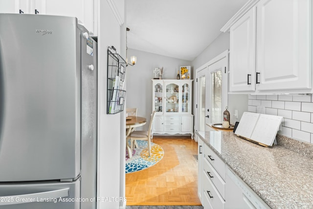 kitchen featuring lofted ceiling, white cabinetry, stainless steel refrigerator, decorative backsplash, and light parquet floors