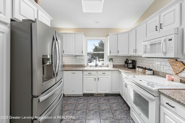 kitchen with vaulted ceiling with skylight, white cabinetry, sink, backsplash, and white appliances