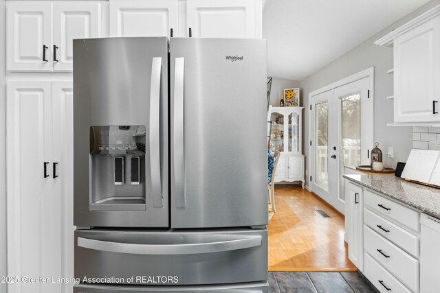 kitchen with dark parquet flooring, light stone counters, stainless steel fridge with ice dispenser, white cabinets, and backsplash