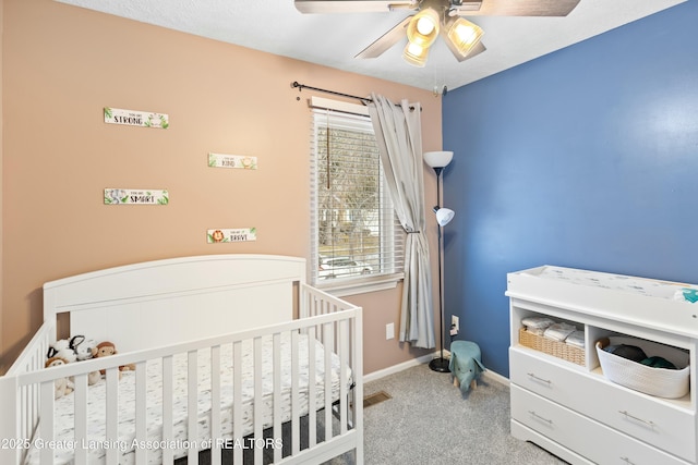 carpeted bedroom featuring ceiling fan and a crib