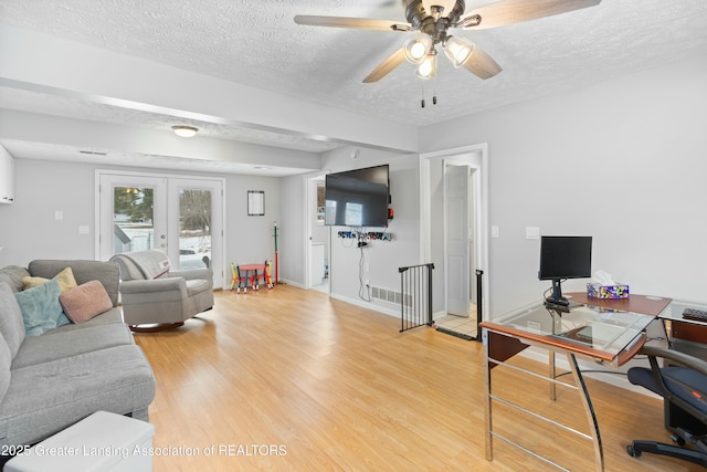 living room with french doors, ceiling fan, wood-type flooring, and a textured ceiling