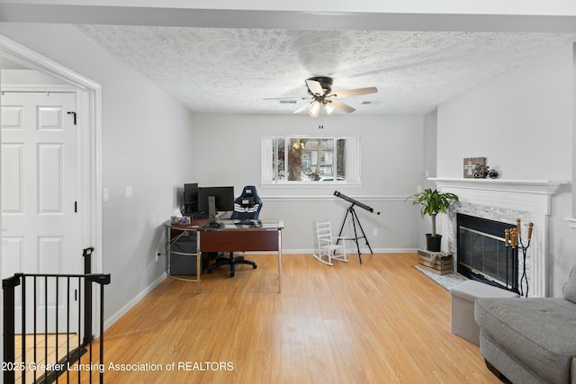 office with a tiled fireplace, ceiling fan, wood-type flooring, and a textured ceiling