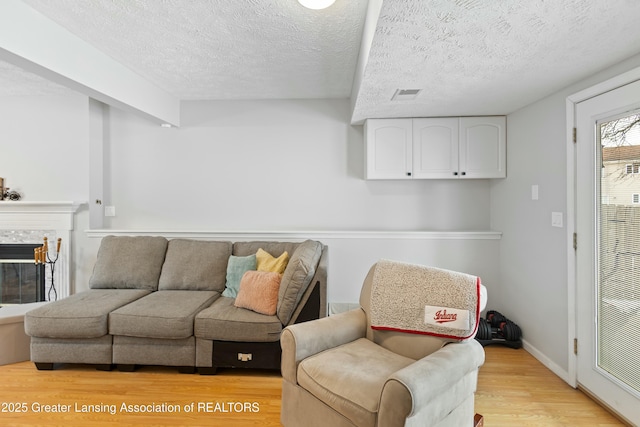 living room featuring a tiled fireplace, light hardwood / wood-style flooring, and a textured ceiling