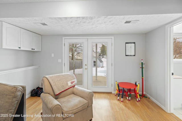 sitting room with french doors, a textured ceiling, and light wood-type flooring