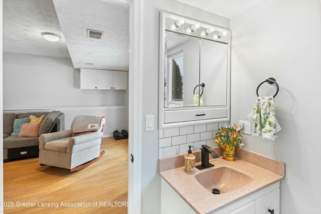 bathroom with vanity, hardwood / wood-style floors, a textured ceiling, and backsplash